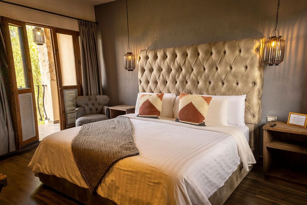 Bedroom with a tufted headboard, king-sized bed, balcony access, and two hanging lamps.