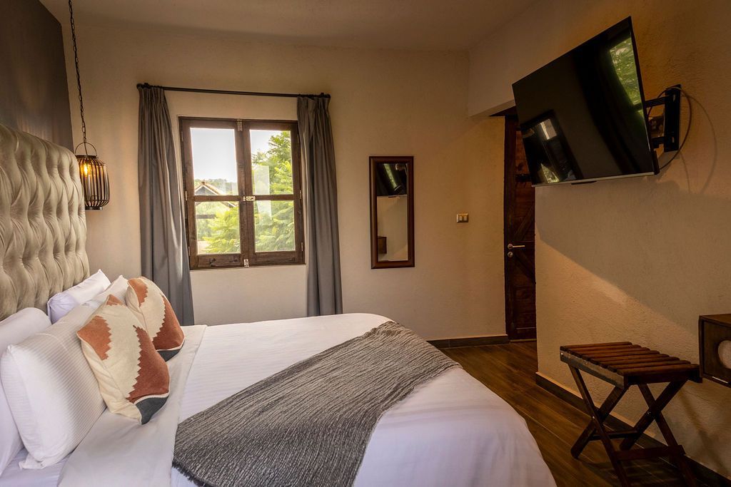 Bedroom with a bed, TV, window, and a small wooden stool.