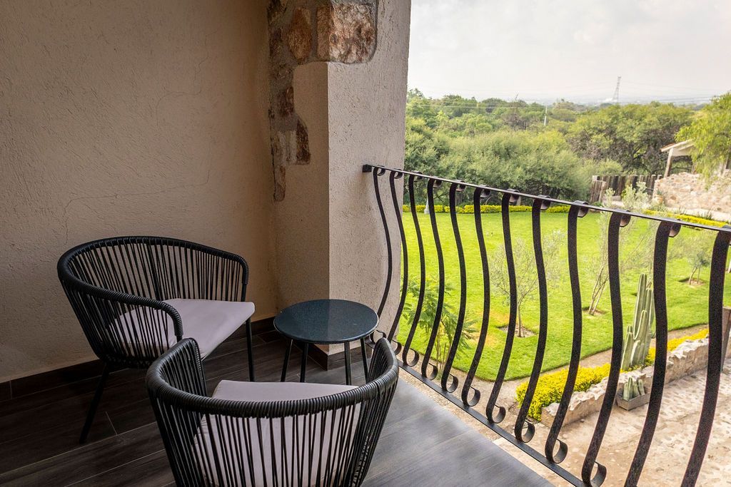 Balcony with two black woven chairs, small table, and a view of green grass and trees.