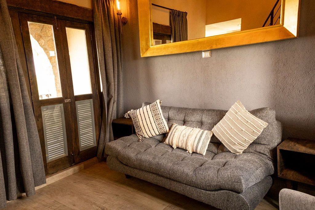 Gray couch with decorative pillows in a room with a mirror, curtains, and doorway.
