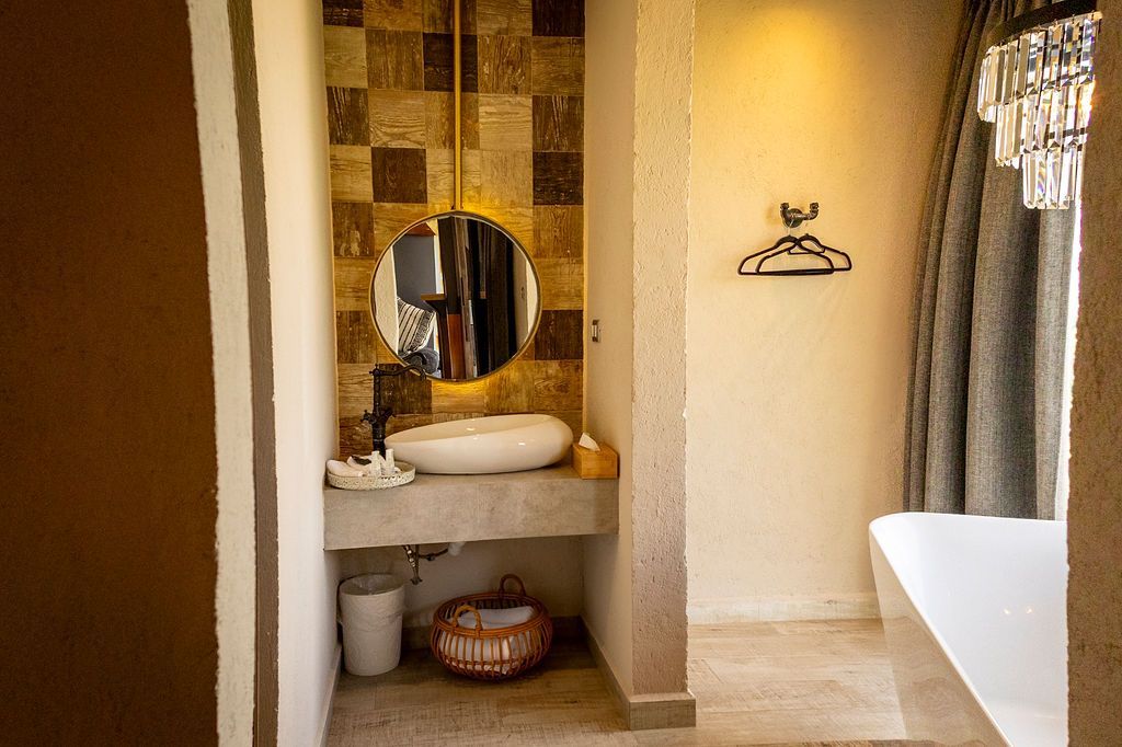 Bathroom with round mirror, stone sink, tiled backsplash, and neutral color scheme.