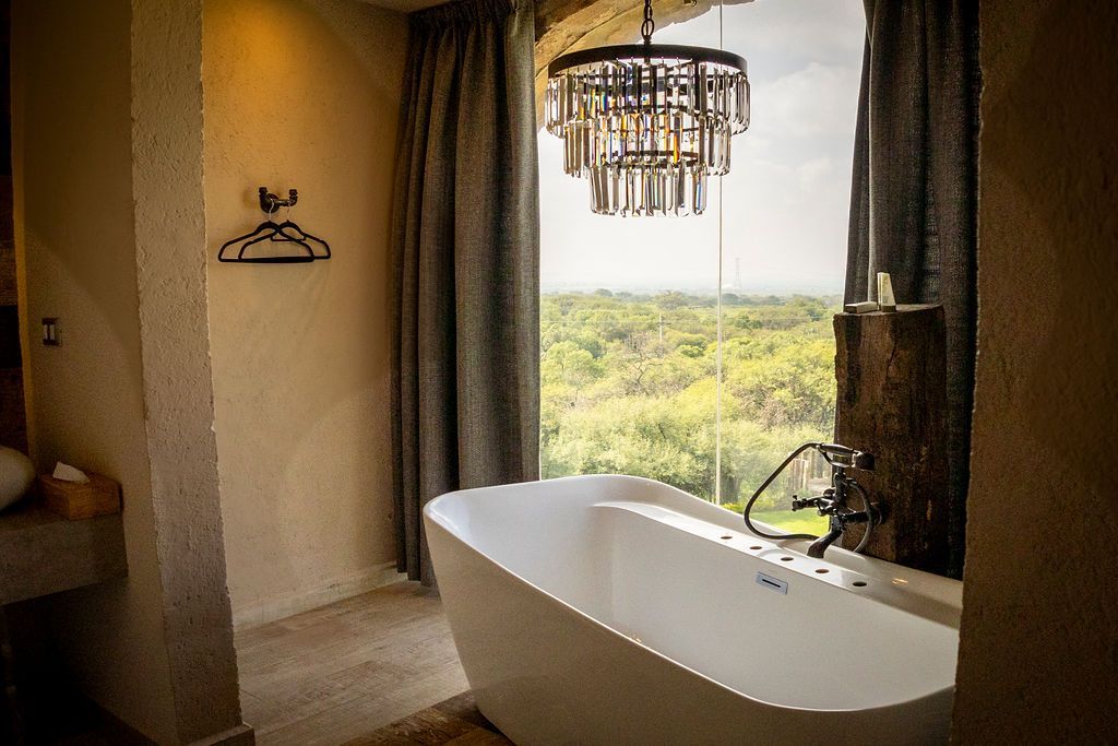 A luxurious bathroom with a freestanding tub, large window, and crystal chandelier.