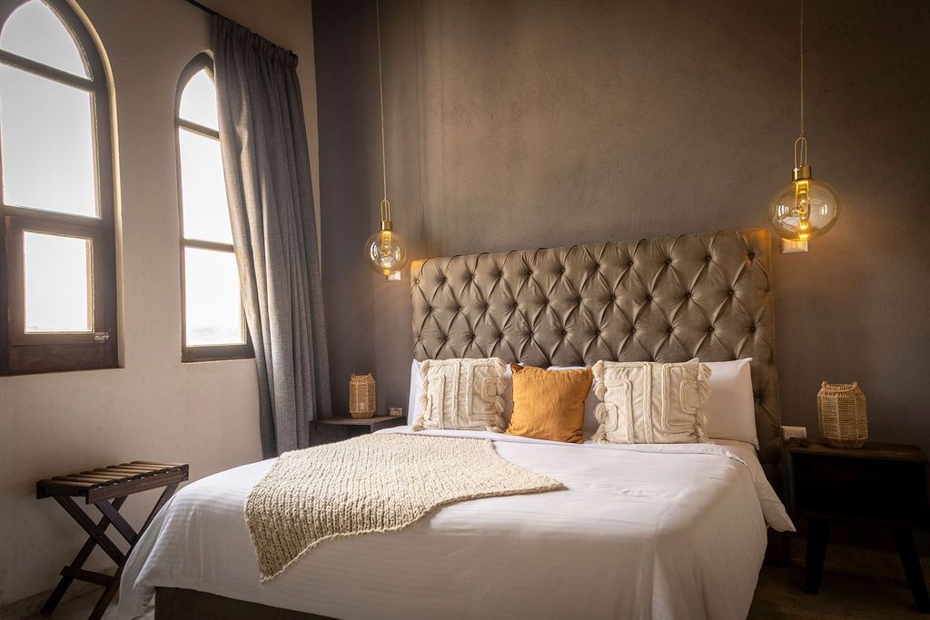 Bedroom with arched window, tufted headboard, and two hanging globe lights.