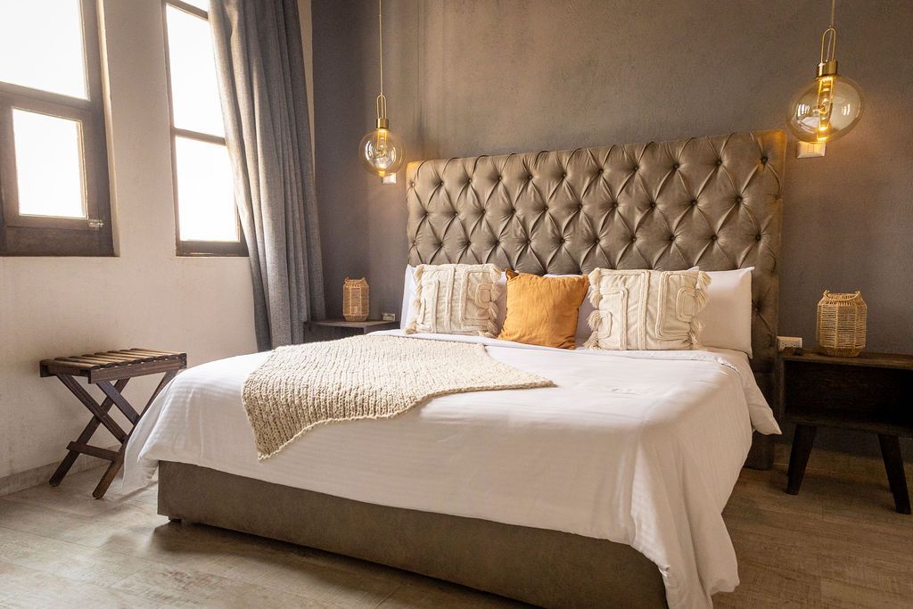 Bedroom with large bed, tufted headboard, side tables, window, and decorative hanging lights.