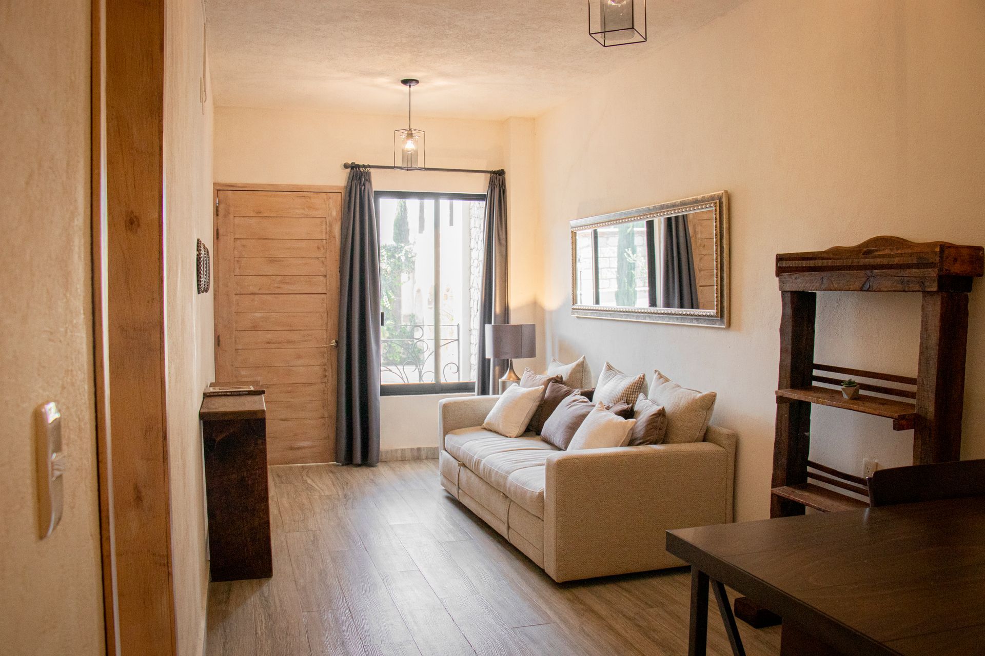 Living room with sofa, window, shelves, and wood door. Beige, gray, and brown tones.