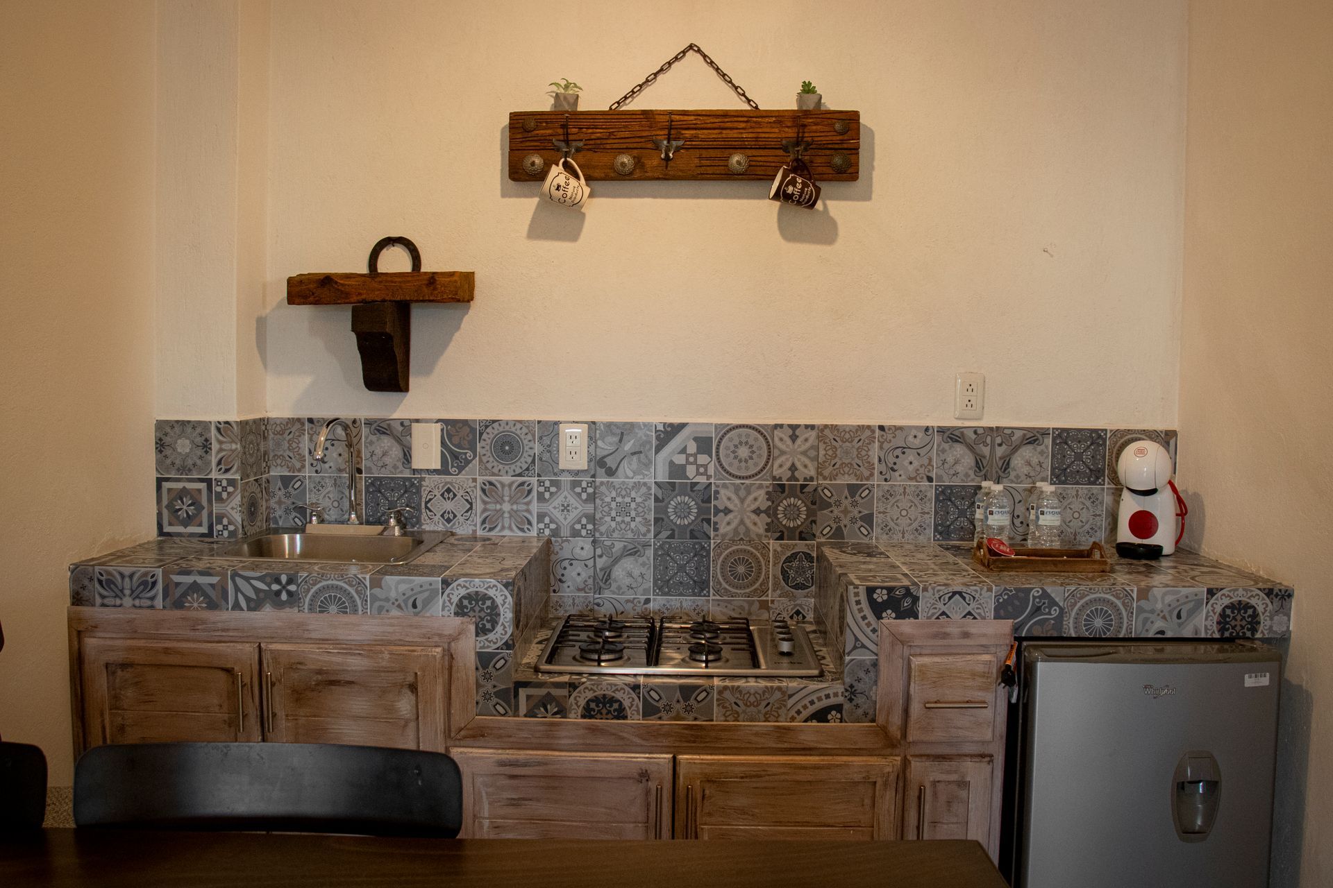 Rustic kitchen with tiled backsplash, wooden cabinets, stovetop, and mini-fridge.