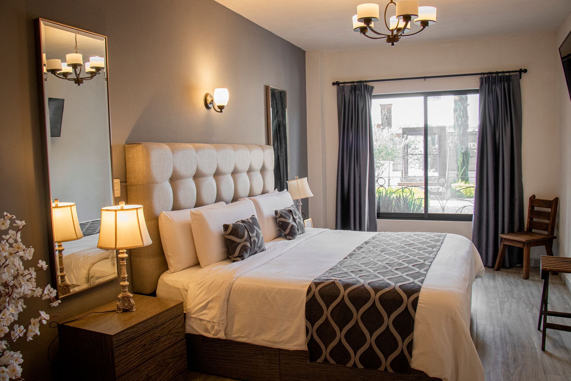 Bedroom with king-sized bed, decorative pillows, lamps, and a window with blue curtains.