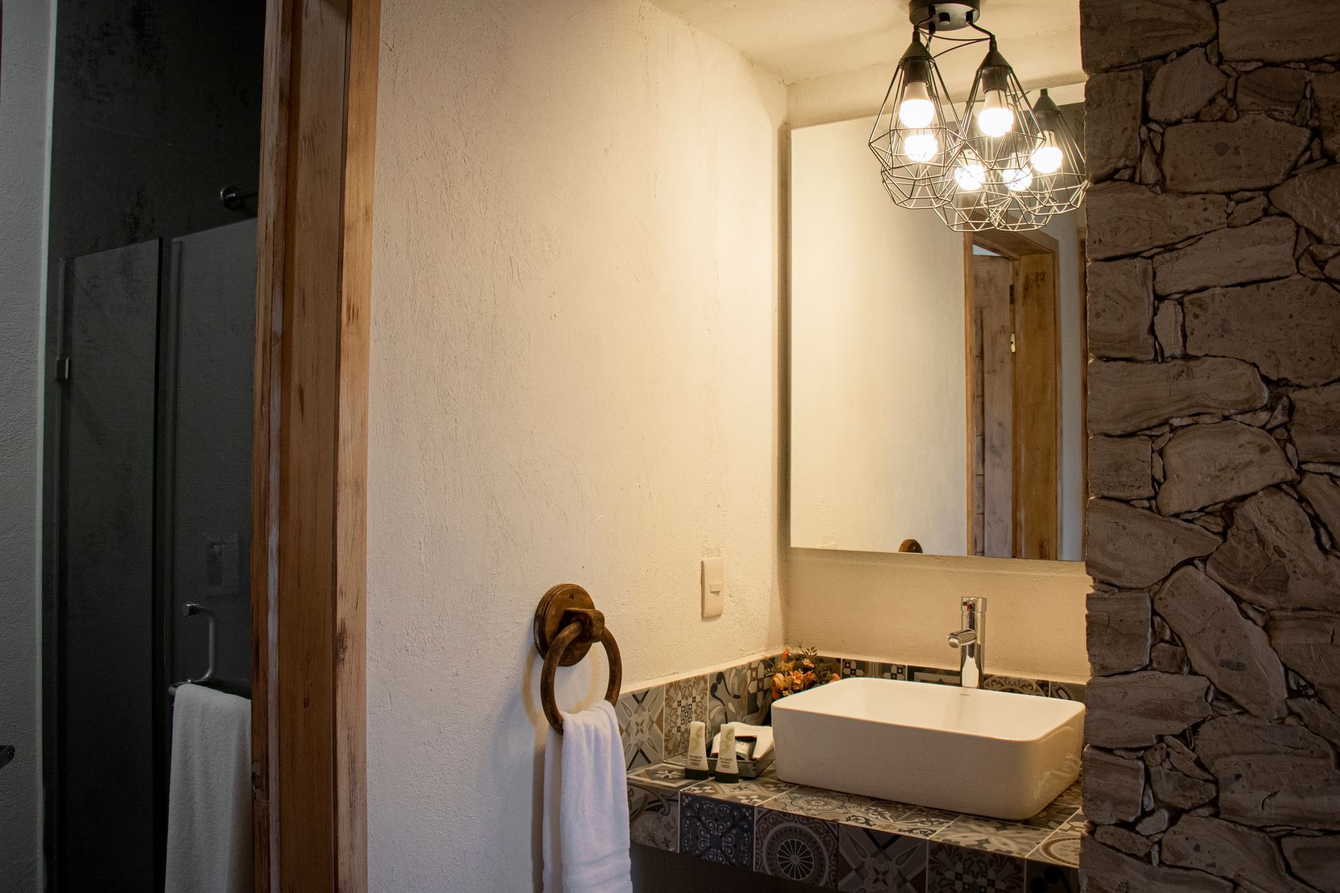 Bathroom with white sink, stone wall, mirror, and decorative light fixture.