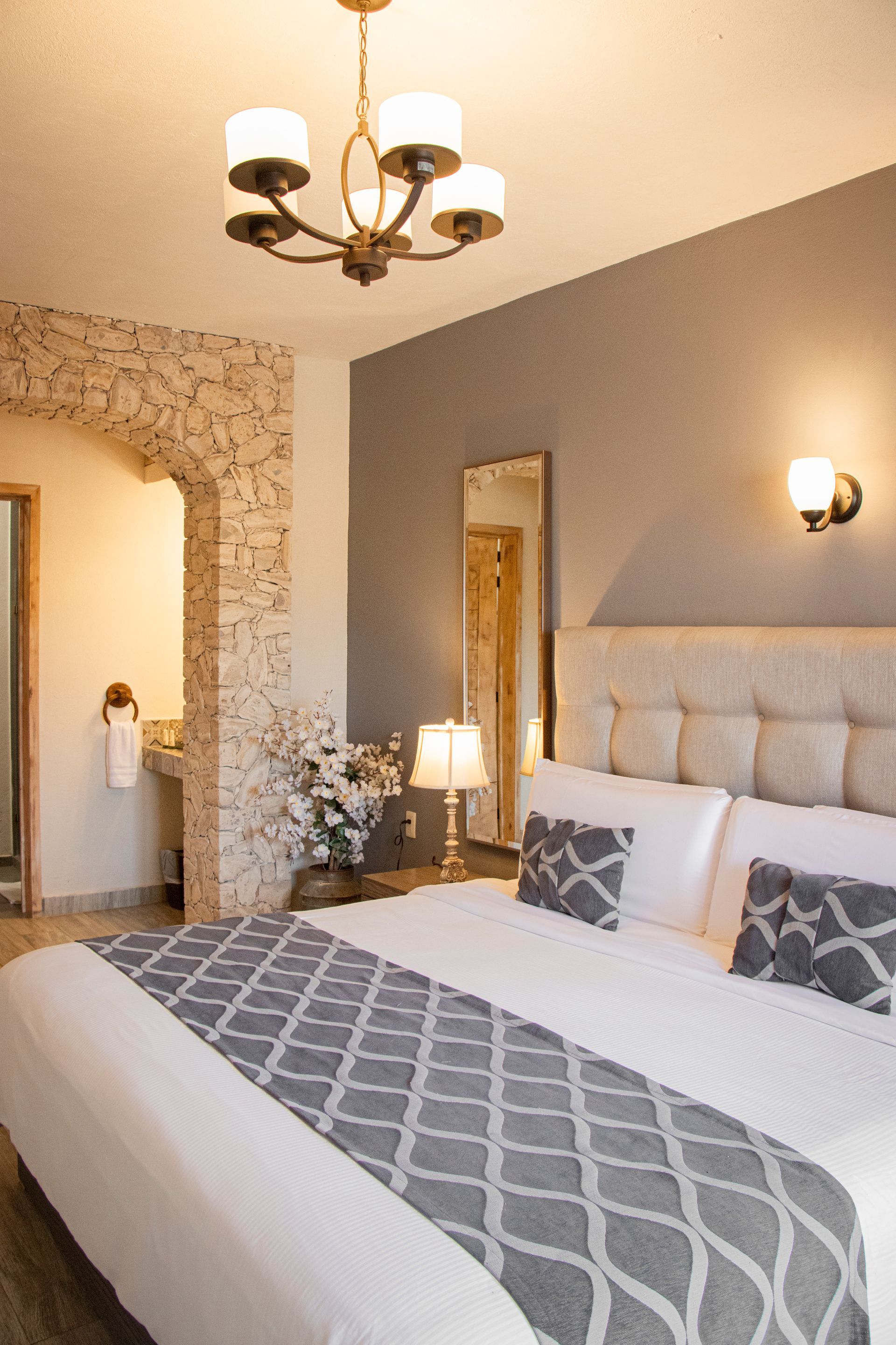 Bedroom with king-sized bed, decorative pillows, gray and white bedding, and stone archway to bathroom.
