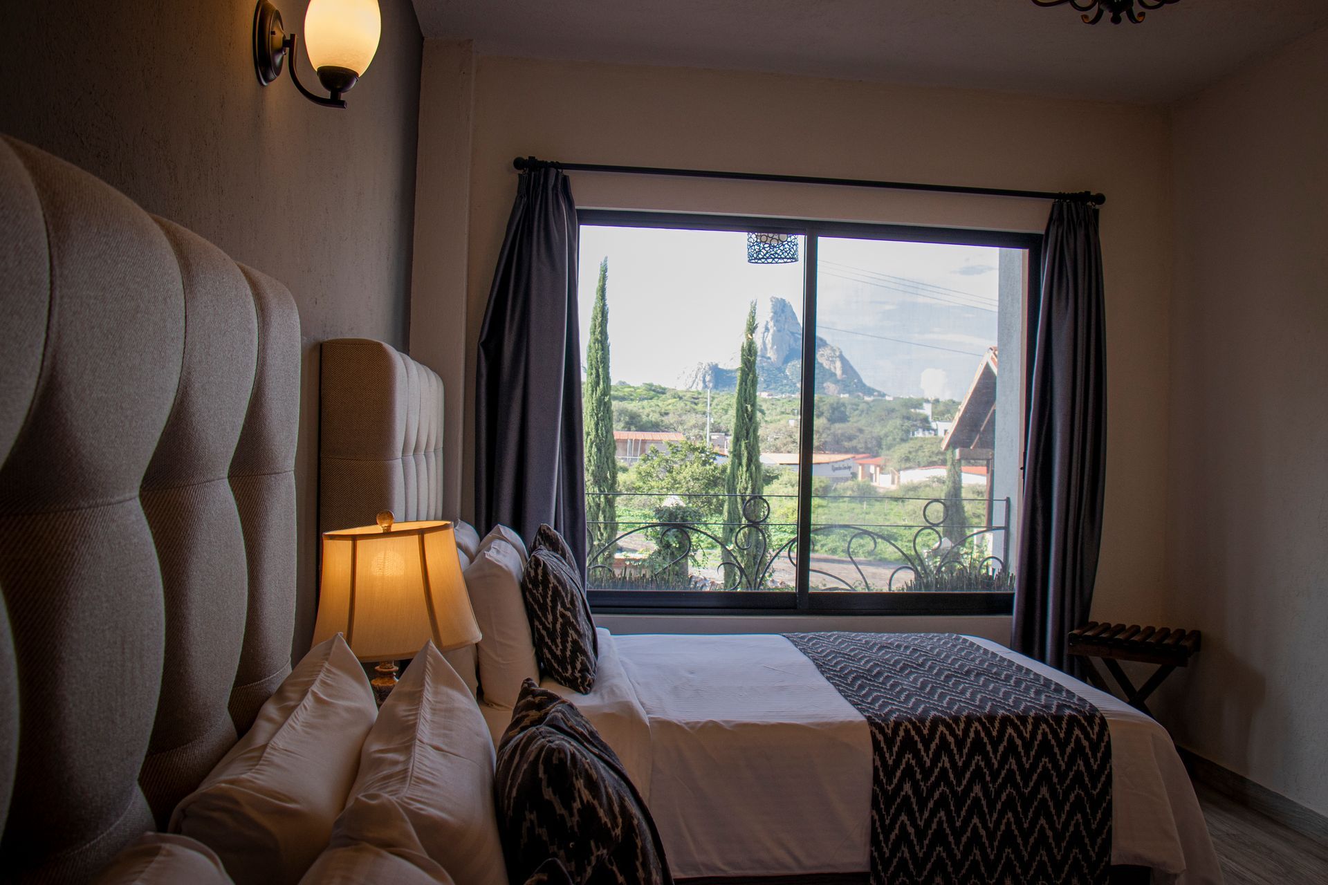 Bedroom with large bed, window overlooking mountain view. Neutral tones, lamp on nightstand.