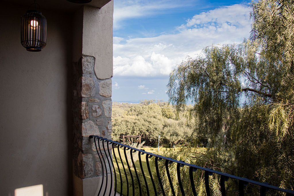 Balcony overlooking trees and field under blue sky, stone wall and black metal railing.