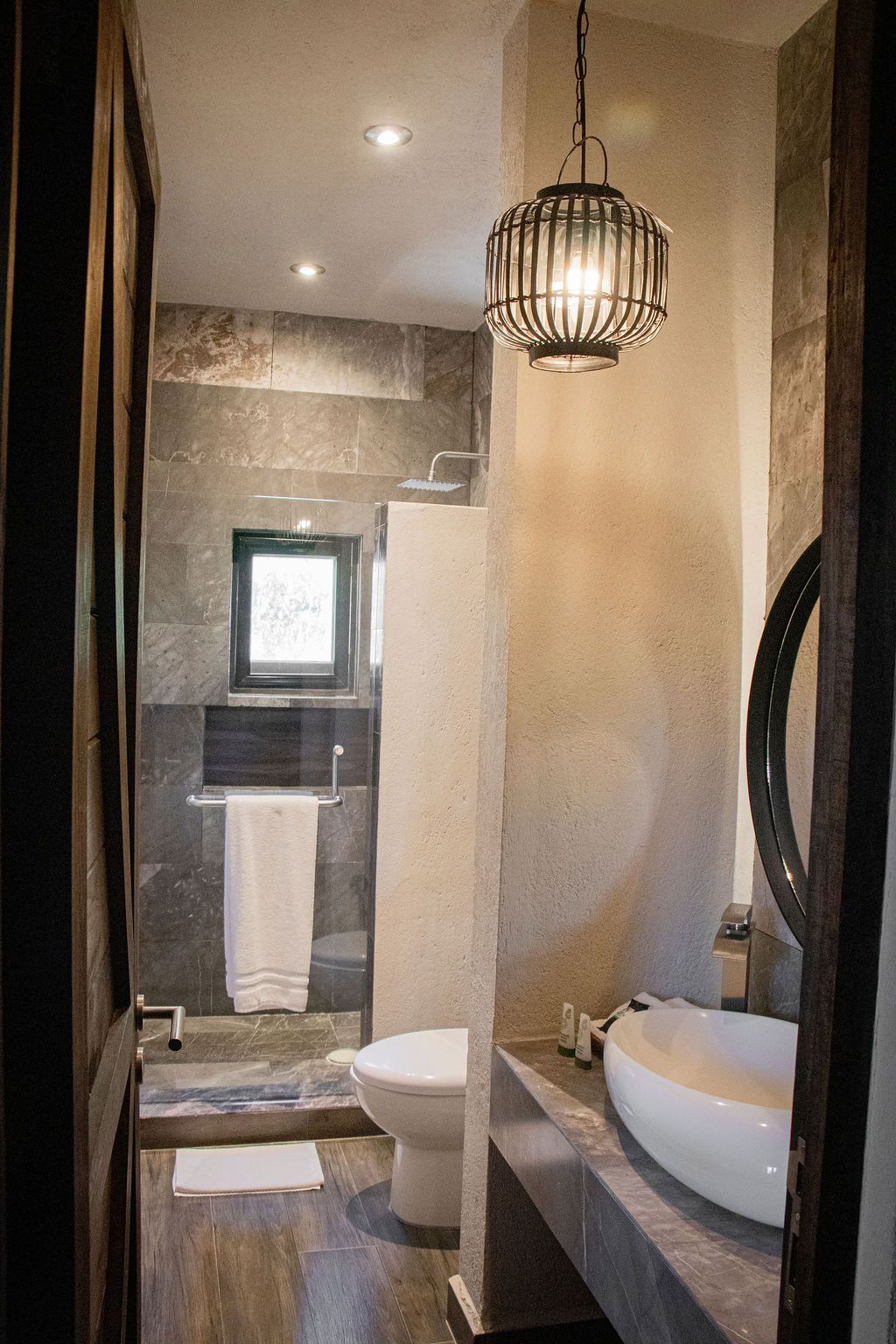 Bathroom with a white sink, toilet, and shower. Dark stone walls, ornate pendant light, and wooden door frame.