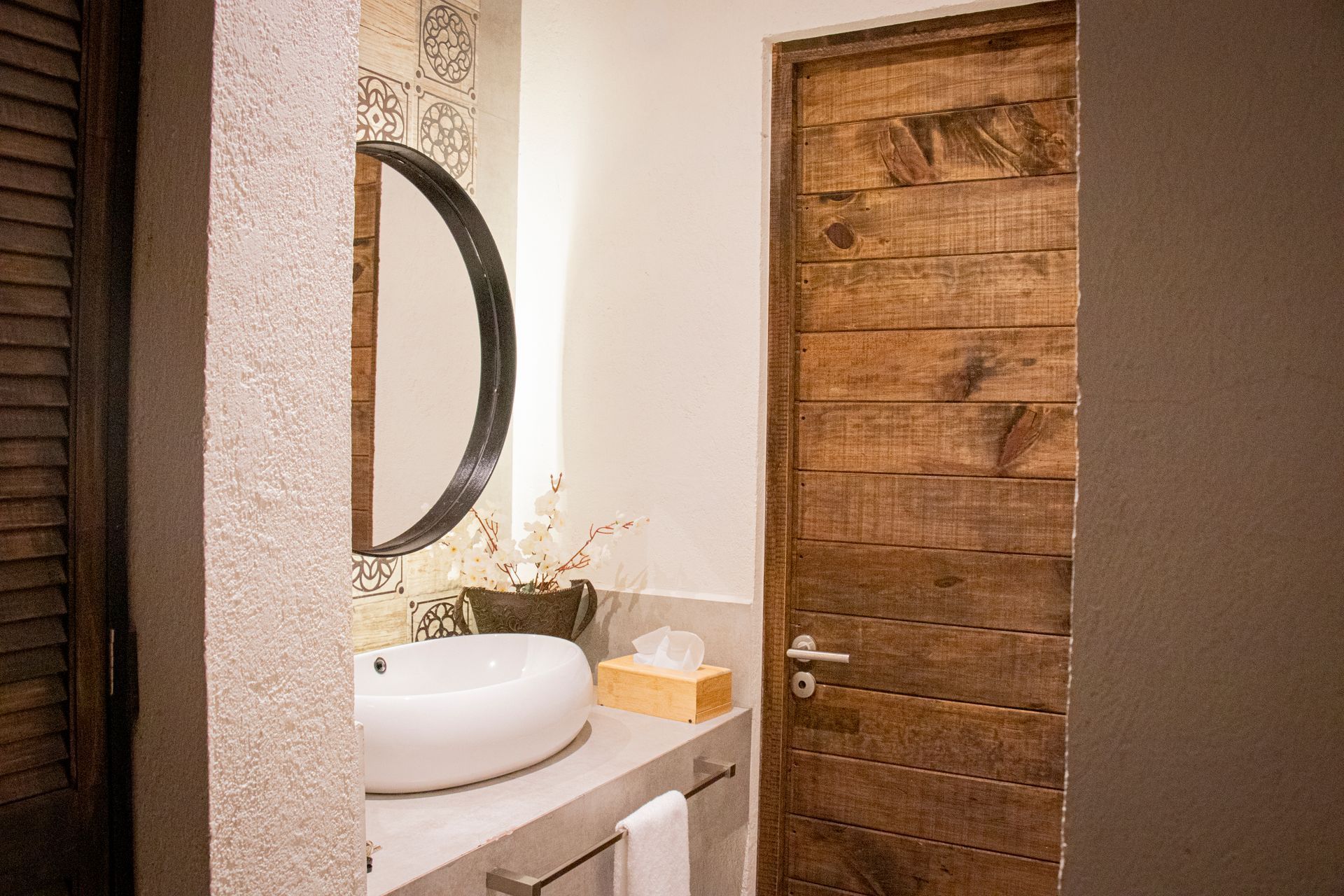 Bathroom with white sink, wooden door, and round mirror.