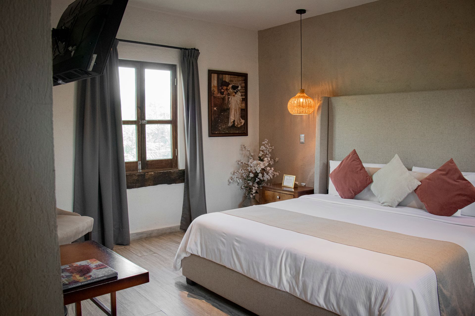 Bedroom with a bed, window, TV, and decorative items. Gray curtains and neutral tones.