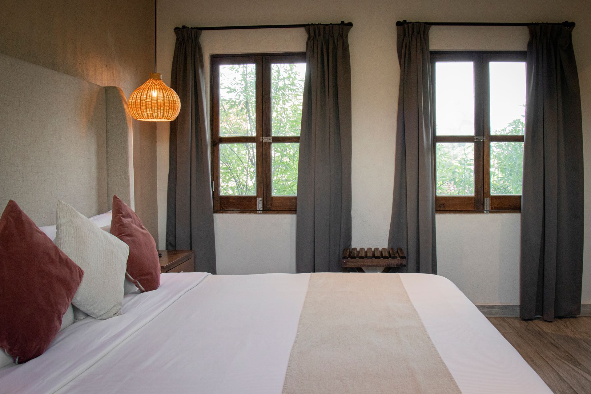 Bedroom with bed, two windows with gray curtains, and a woven pendant light.