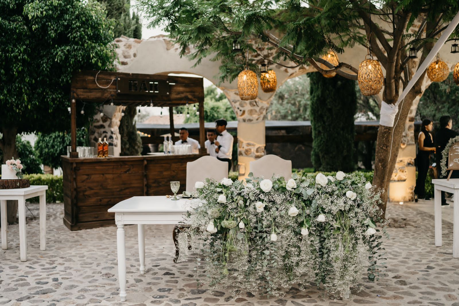Outdoor wedding reception with a bar, white tables, and floral decorations.