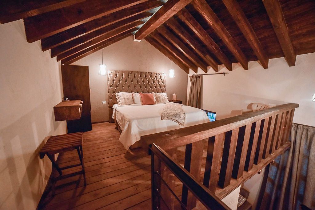 Bedroom loft with wooden beams, railing, and a large bed with a tufted headboard.