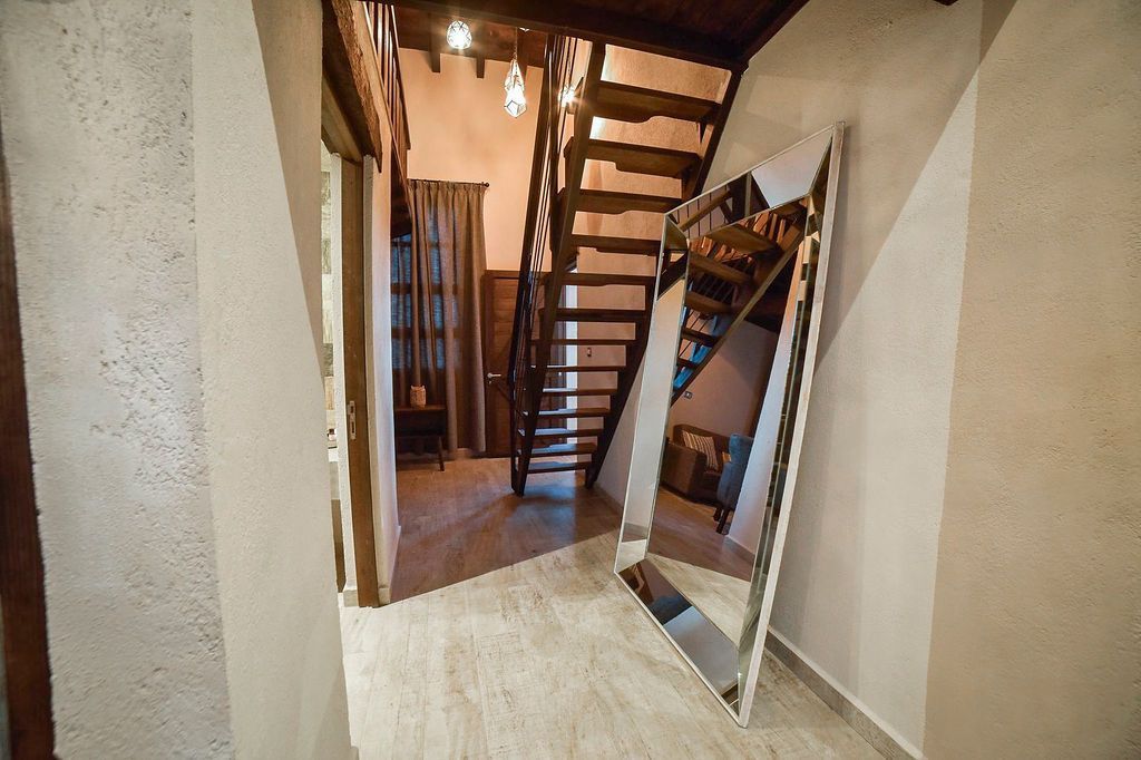 Hallway with wooden staircase, large angled mirror, beige walls, and wood flooring.