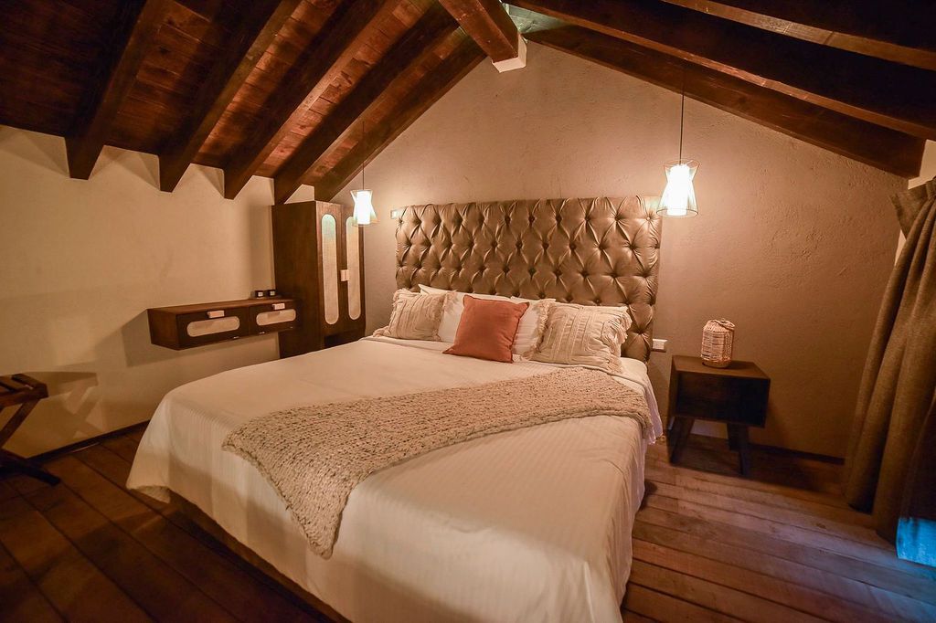 Bedroom with a large bed, plush headboard, wooden ceiling and floor, and bedside tables.