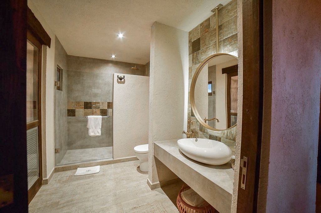 Bathroom with stone walls, shower, oval sink, and large round mirror.