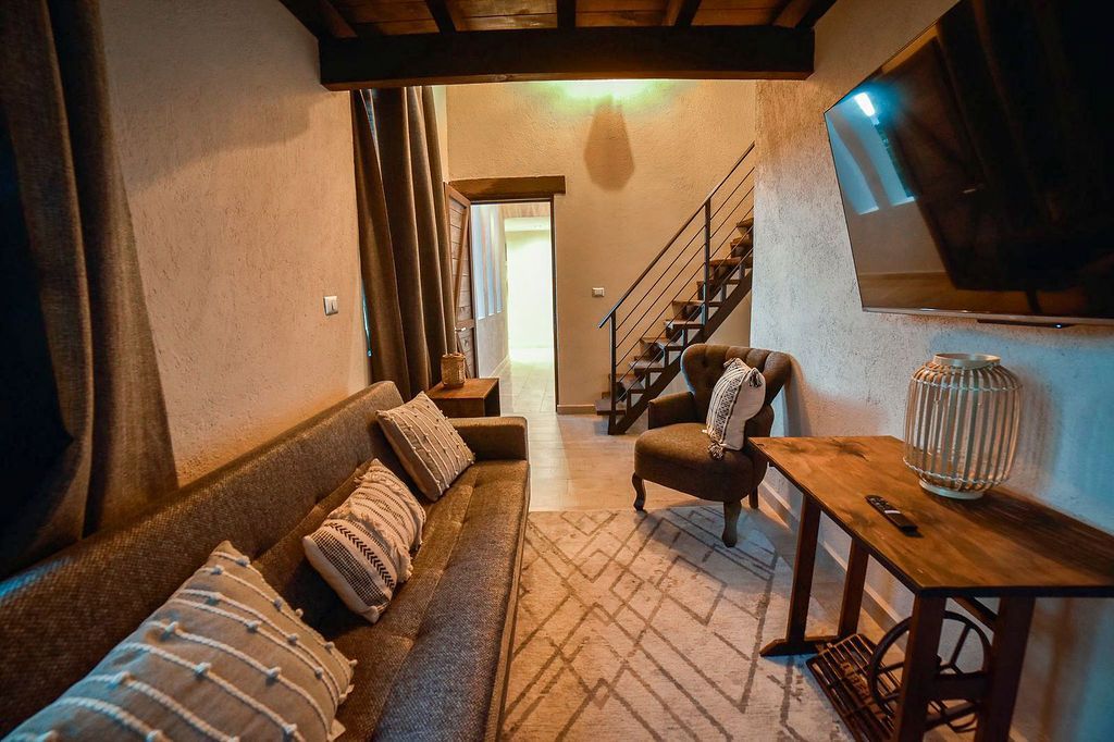 Cozy living room with a couch, armchair, rug, and wooden side table. A staircase leads upstairs.