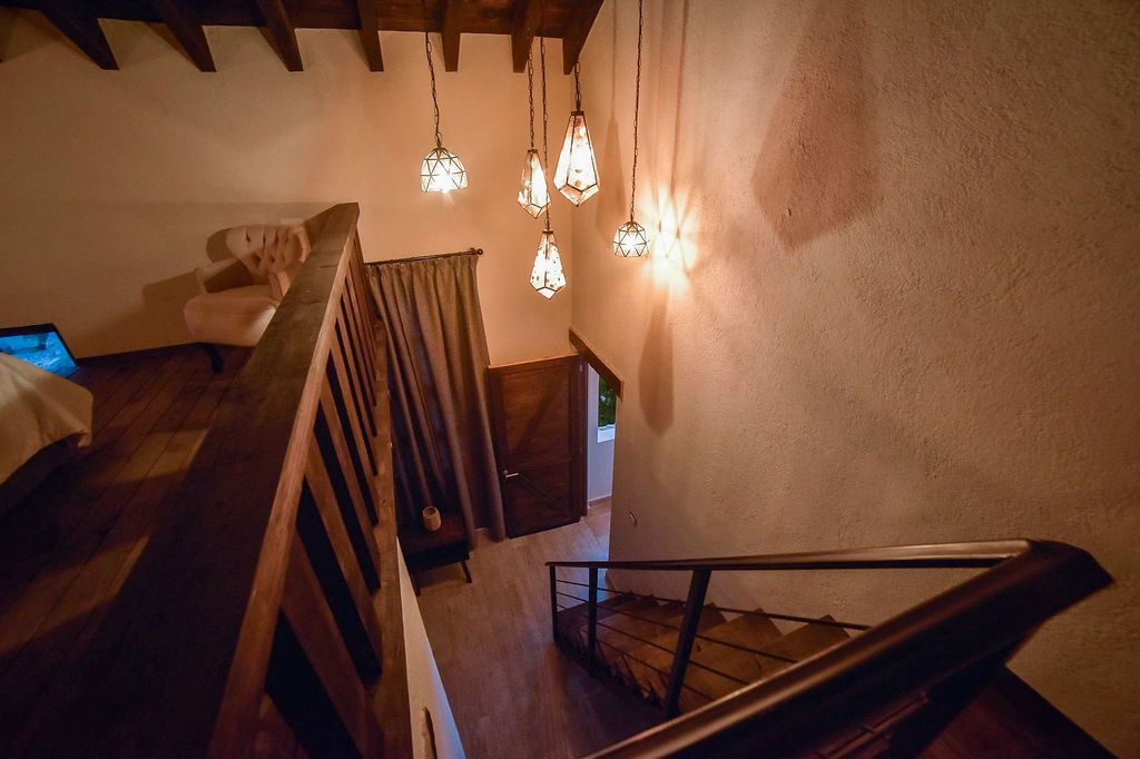 Wooden staircase with hanging lights, leading down to a door and window. Soft lighting.