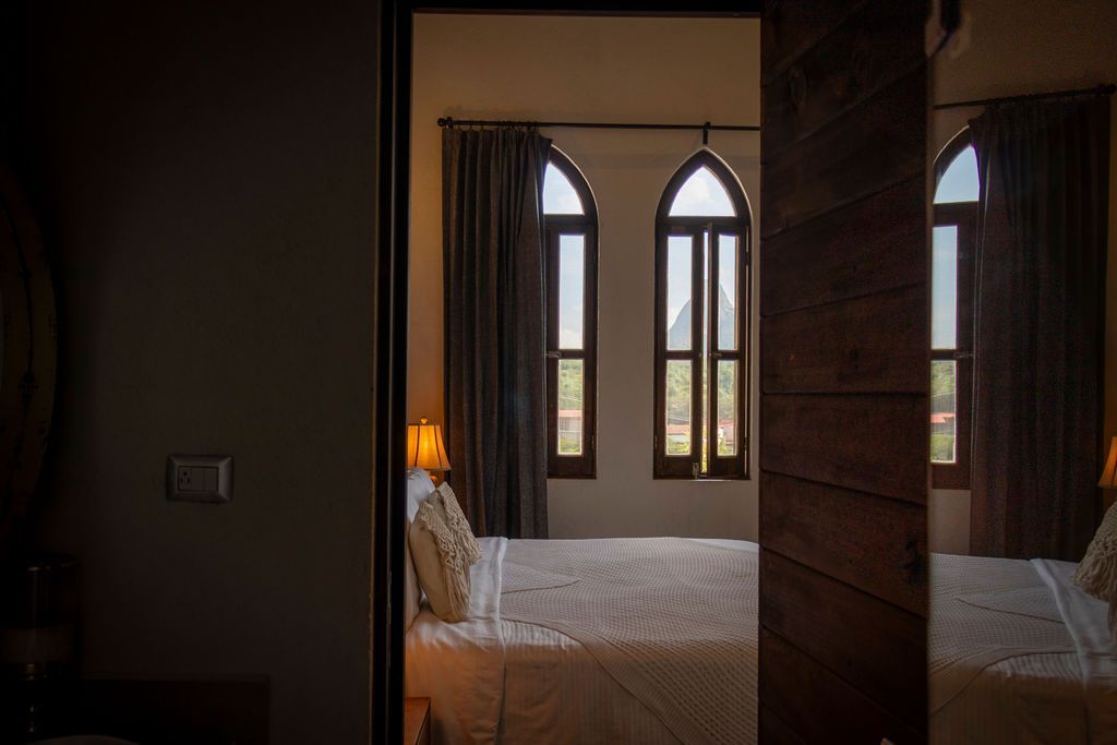 Bedroom interior seen through doorway with arched windows, bed, and curtains.