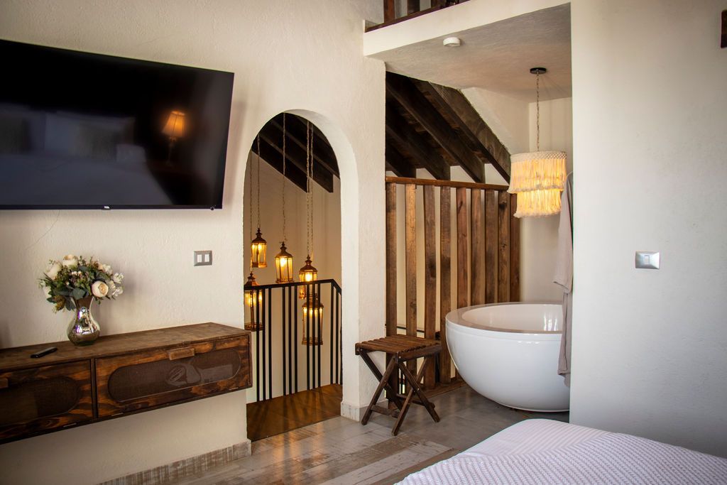 Bedroom with a TV, a wood cabinet, stairs, and a tub behind wooden slats.