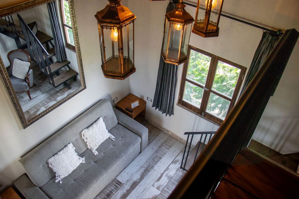 Overhead view of a small living area. Gray sofa, mirror with stairs, wood trim, hanging lanterns.