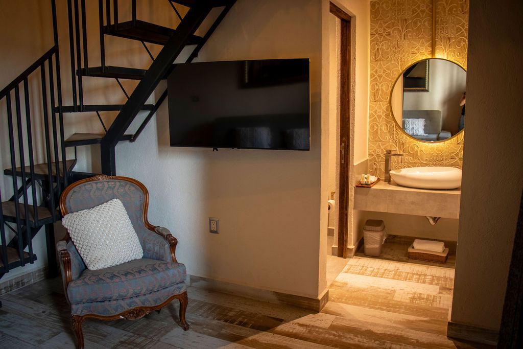 Cozy room with staircase, chair, TV, and bathroom with a round mirror and vessel sink.