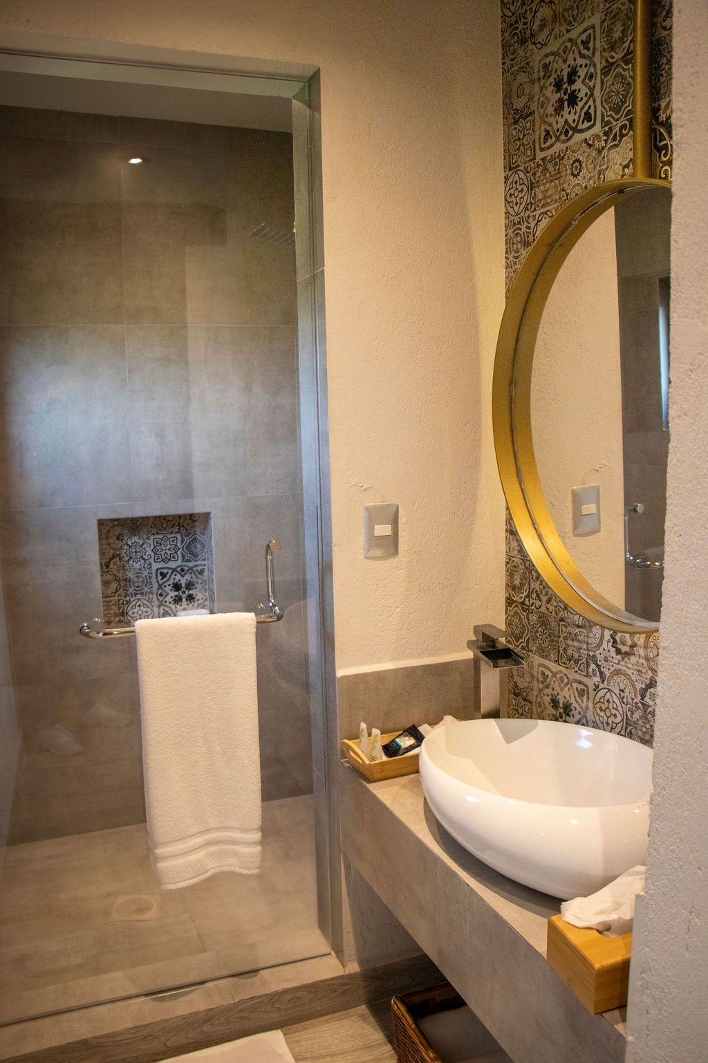 Bathroom with shower, sink, and decorative tile. Gold mirror, white sink, gray walls, towel hanging.