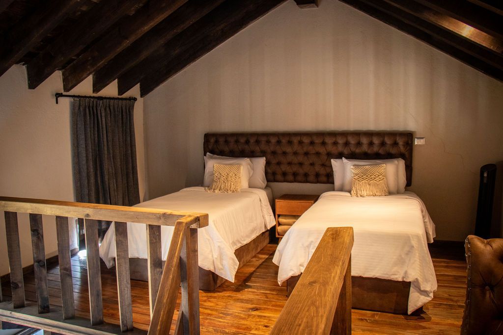 Two twin beds with white linens in a loft bedroom, wooden beams and railing visible.