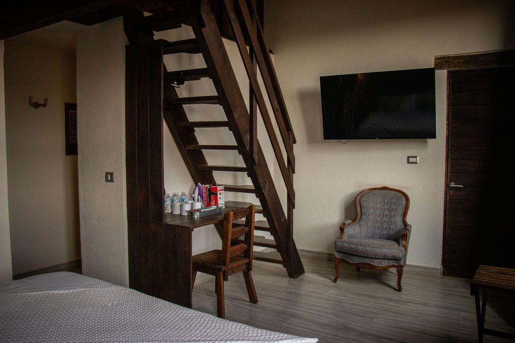 Bedroom interior with wooden staircase, small desk, chair, armchair, and a wall-mounted TV.