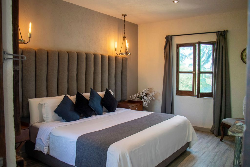 Bedroom with large bed, gray headboard, pillows, gray accents, and window with curtains.