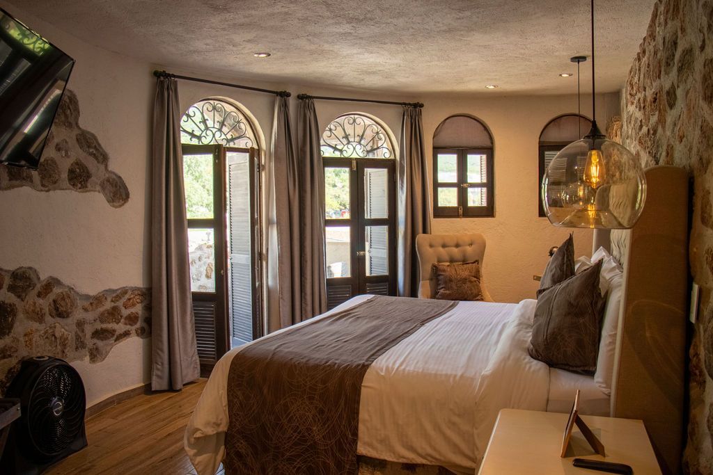 Bedroom with a king-size bed, stone walls, arched windows, and decorative pendant lights.