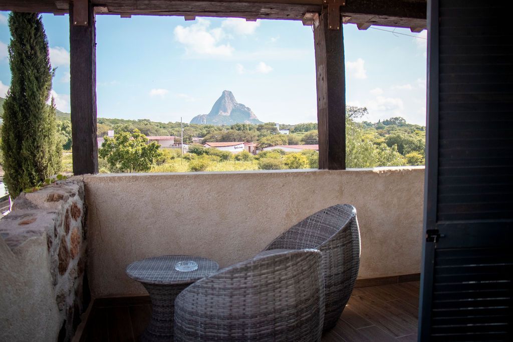 Balcony with wicker chairs, small table, scenic mountain view.
