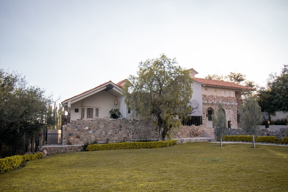 House with stone facade and red-tiled roof, set on a grassy lawn with trees and a light-blue sky.
