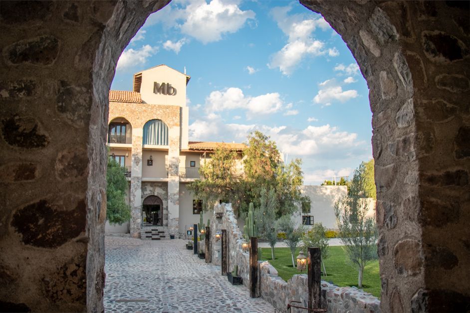 Stone archway frames a hotel building under a blue sky with clouds.