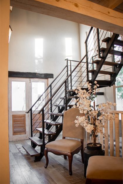 Staircase with black metal railing and wooden steps, leading up to a second floor. A chair sits below.