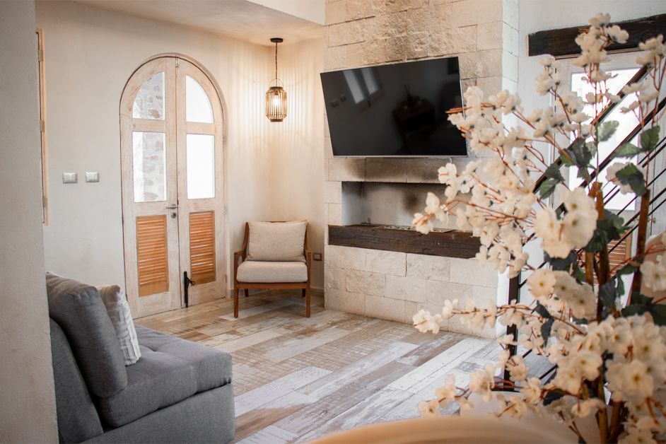 Living room with TV on stone wall, a chair, sofa, and faux flower arrangement.