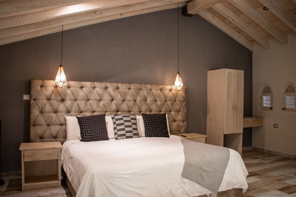 Bedroom with king-sized bed, tufted headboard, bedside tables, wardrobe, and pendant lights. Gray walls, light wood ceiling and floor.