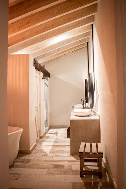 Bathroom with angled ceiling, wood beams, light wood floors, and a freestanding tub.