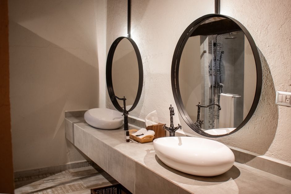 Bathroom with two oval mirrors above white sinks, gray countertop, and neutral-colored walls.