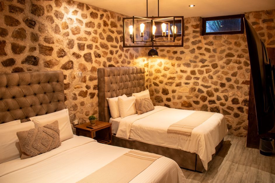 Two beds in a room with stone walls, lit by a chandelier and wall sconce.