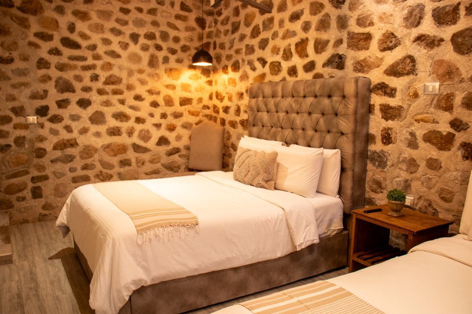 Bedroom with stone walls, two beds, plush headboards, and wooden nightstand with lamp.