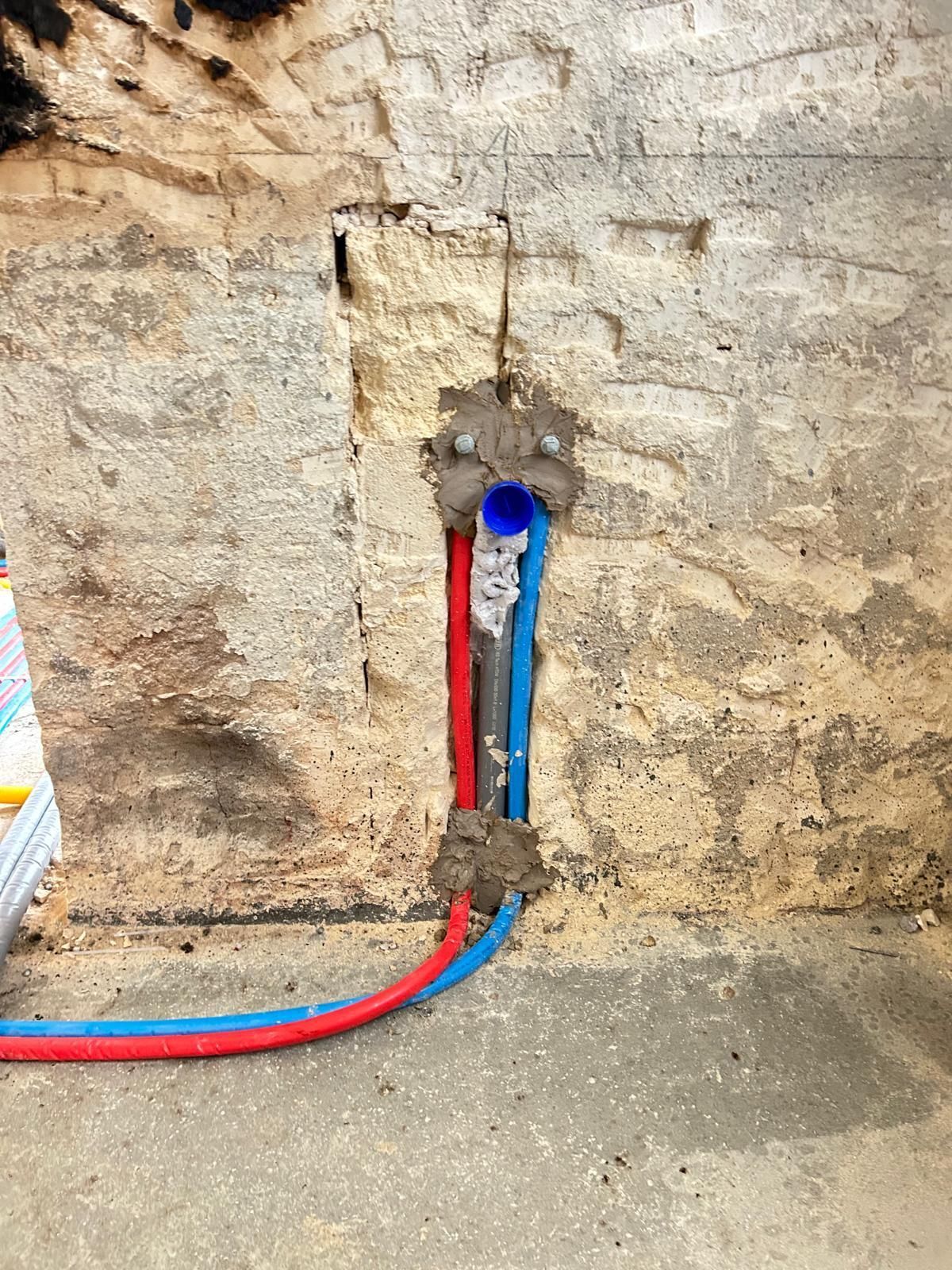 Tubi rossi e blu che fuoriescono da un'apertura in un muro grezzo vicino a un pavimento di cemento.