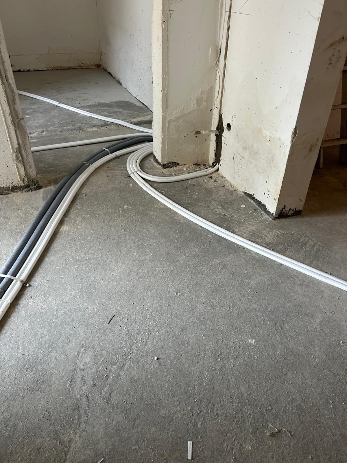 Cavi elettrici che serpeggiano su un pavimento di cemento nudo vicino a una porta e all'angolo di una parete.