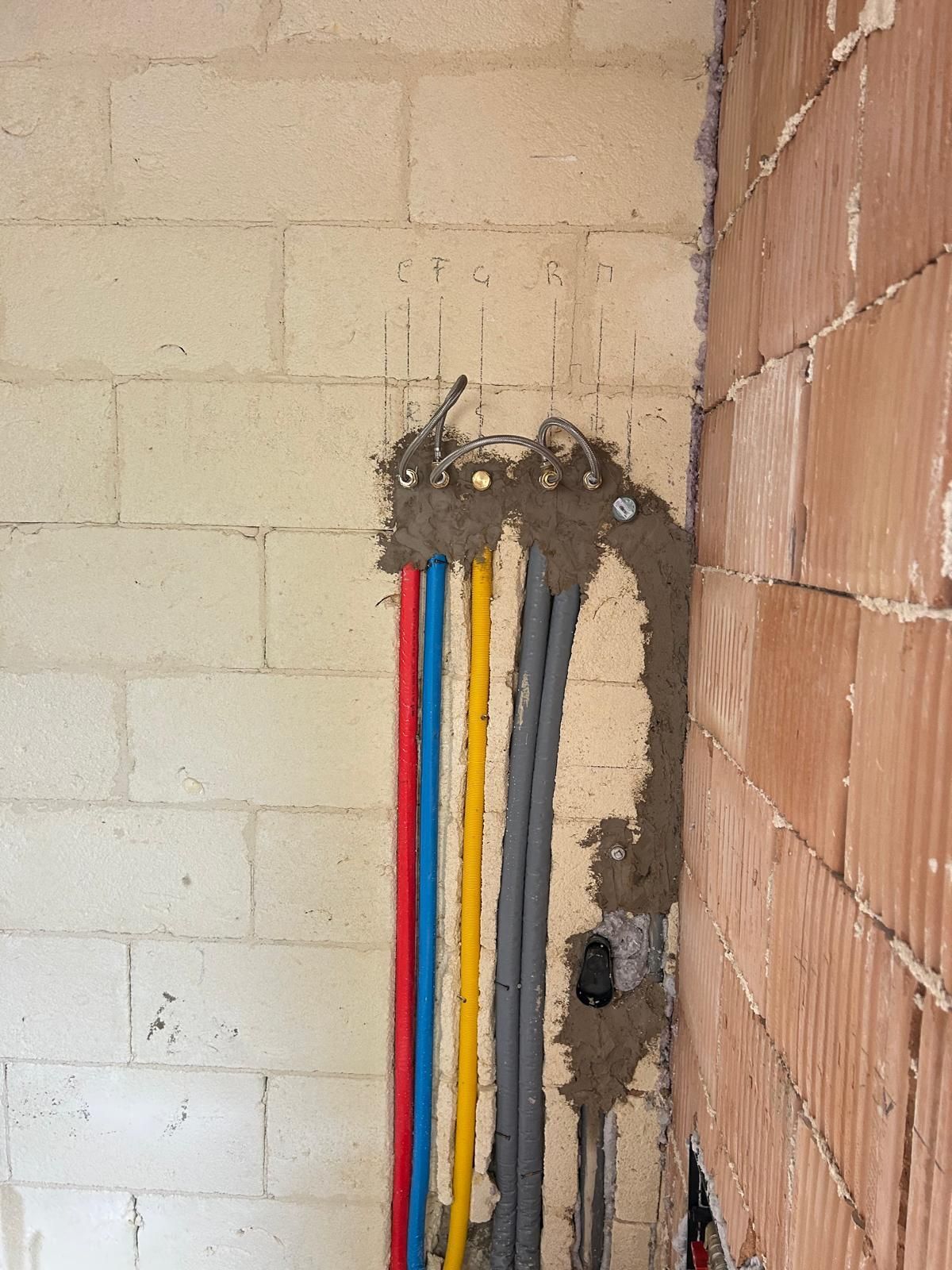 Cavi colorati a vista che fuoriescono da un'apertura nel muro accanto a una parete di mattoni in un cantiere.