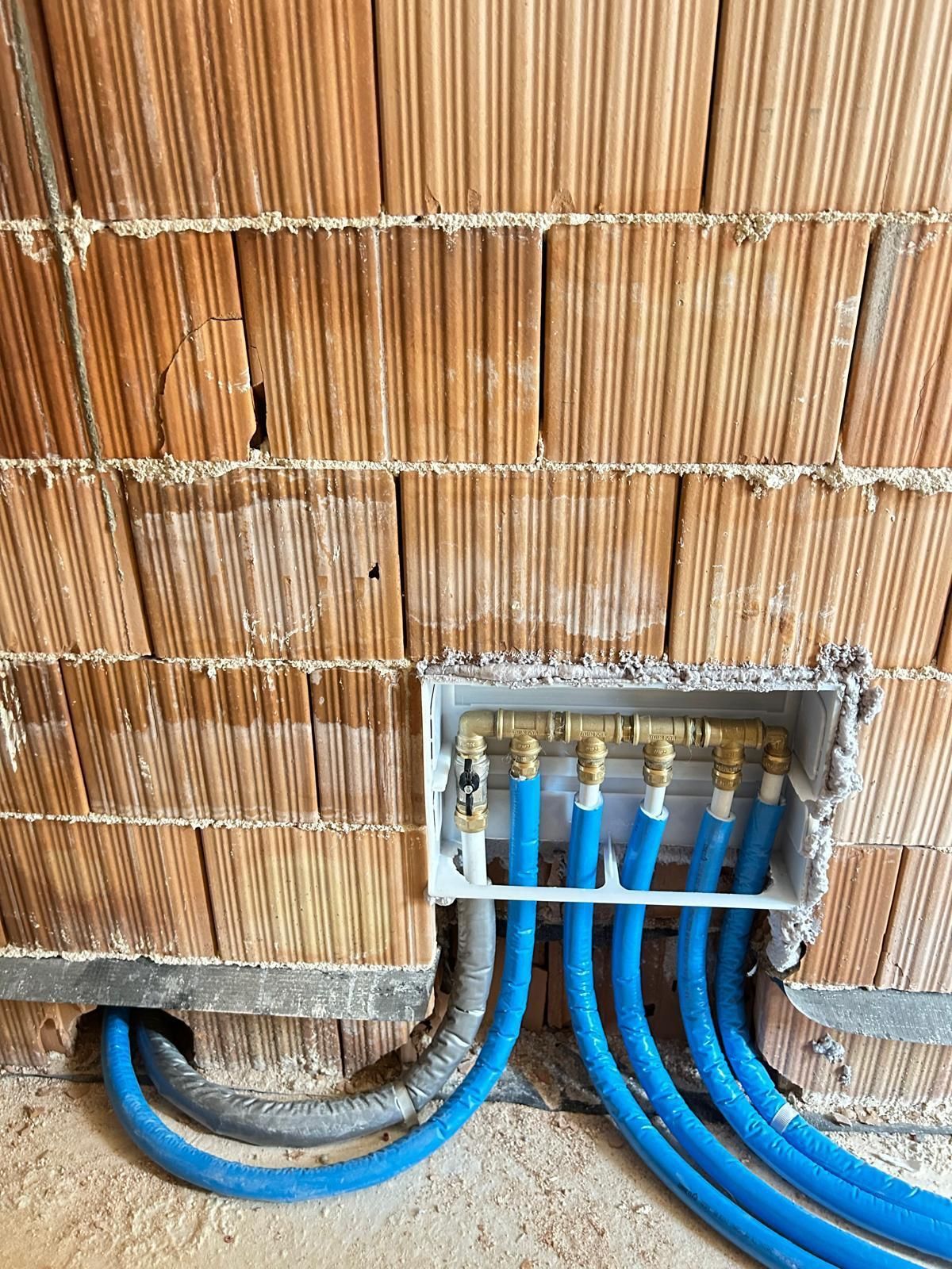 Cablaggio elettrico all'interno di una parete, con cavi blu che entrano in una scatola di derivazione metallica a ridosso di un muro di mattoni non rifinito.