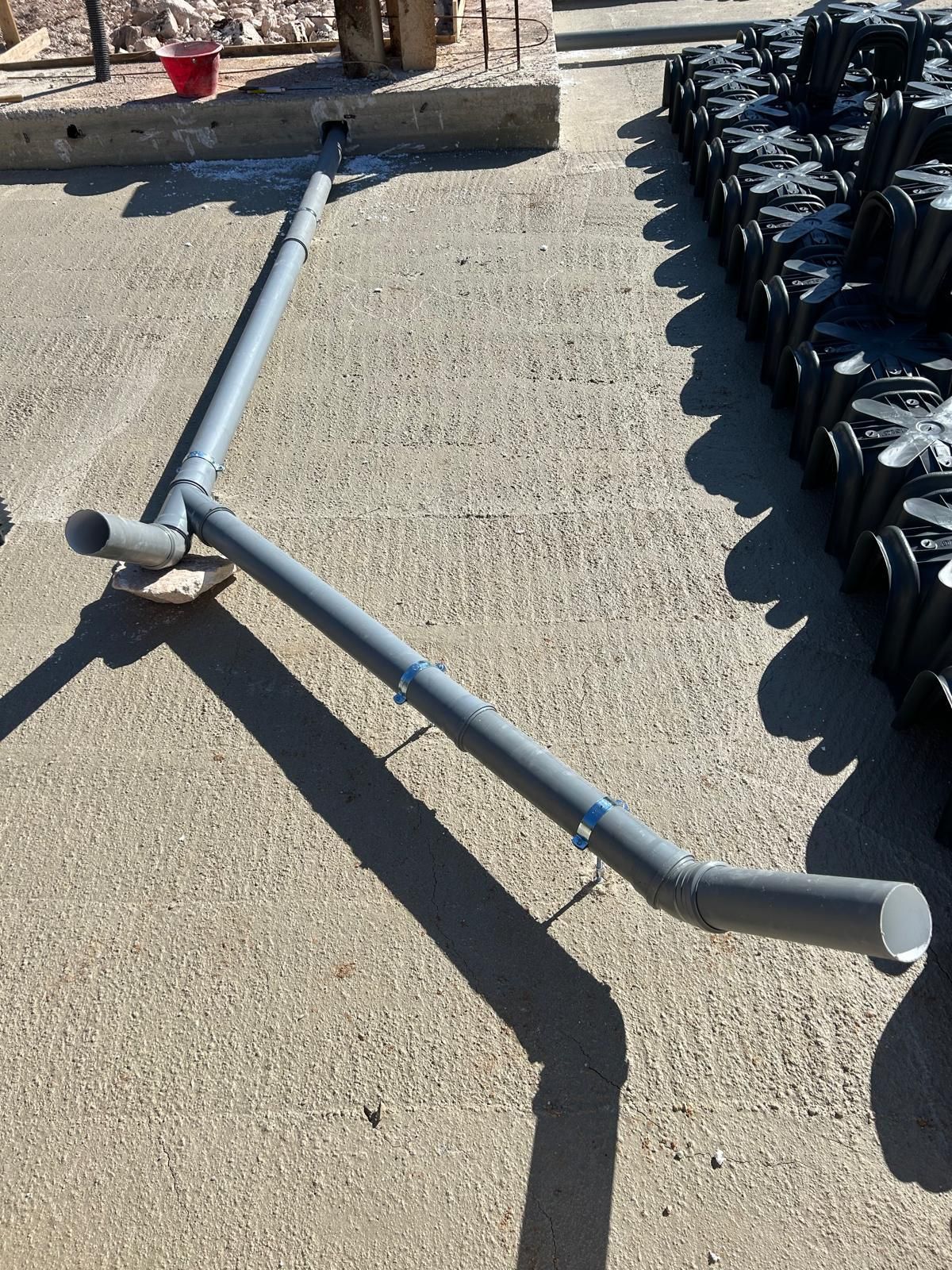 Assemblaggio di tubi in PVC grigio posato su una superficie di ghiaia accanto a sacchi neri impilati all'aperto